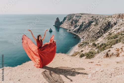 Woman red dress sea. Female dancer posing on a rocky outcrop high above the sea. Girl on the nature on blue sky background. Fashion photo.