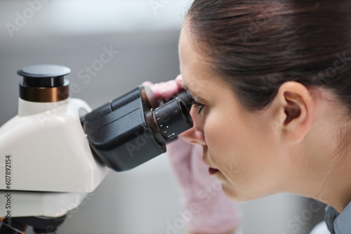 Side view closeup of female scientist looking in microscope while doing research in laboratory