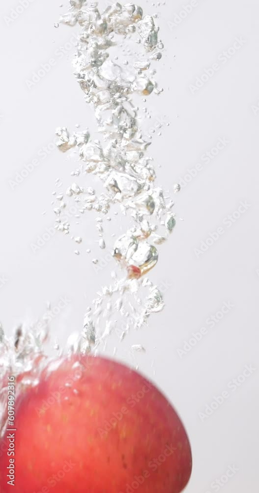 Vertical video 4K footage Front view SLO MO CU, fresh red apple fruit falling into the water splashing. 