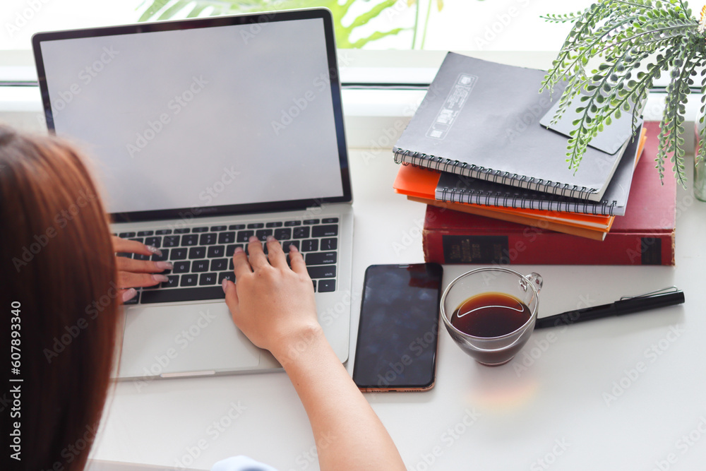 Fototapeta premium Young Asian businesswoman using laptop and notebook computers to work through internet to collect and organize investment documents. young businesswoman concept using technology to help investment