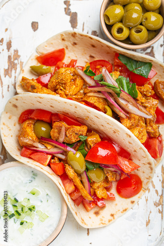 Traditional Greek Dish Gyros: Pita bread Wraps with vegetables, meat, herbs, olives on rustic wooden cutting board with Tzatziki sauce, olive oil top view, white wooden background, closeup.