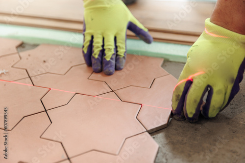 Tiler placing ceramic floor in bathroom tile in position over adhesive with lash tile laser leveling system. Process ceramic Tiles