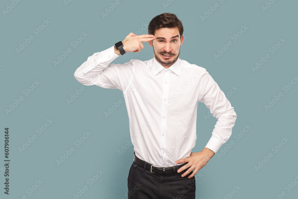 Portrait of depressed attractive man with mustache holding fingers gun near his temple, being in bad mood and stress, wearing Indoor studio shot isolated on light blue background. Portrait of depressed attractive man with mustache holding fingers gun near his temple, being in bad mood and stress, wearing Indoor studio shot isolated on light blue background.