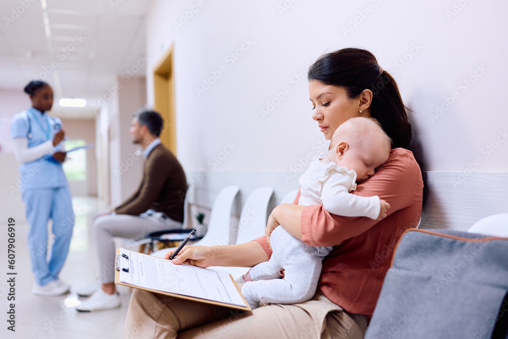 Single mother with baby filling out paperwork in waiting room at pediatrician's. Single mother with baby filling out paperwork in waiting room at pediatrician's.