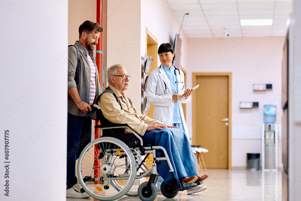 Smiling man pushing his senior father in wheelchair after medical examination at clinic. Smiling man pushing his senior father in wheelchair after medical examination at clinic.