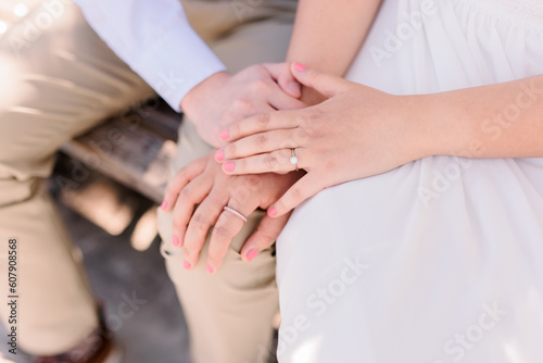 An engaged couple are holding hands, her hand is on top of his. 