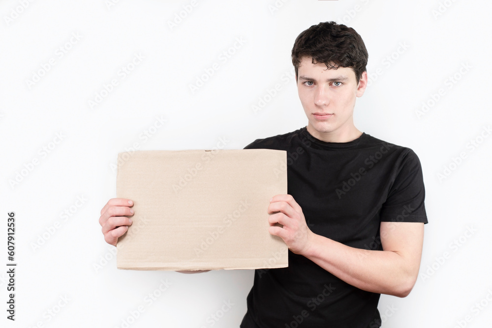 A young guy is just starting his career and looking for a job, holding a sign in his hands with a place for text, the guy is humble, doubting his abilities A young guy is just starting his career and looking for a job, holding a sign in his hands with a place for text, the guy is humble, doubting his abilities