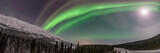 Panoramic landscape aurora borealis views in northern Canada, Yukon Territory during winter time with bright northern lights covering the sky. 