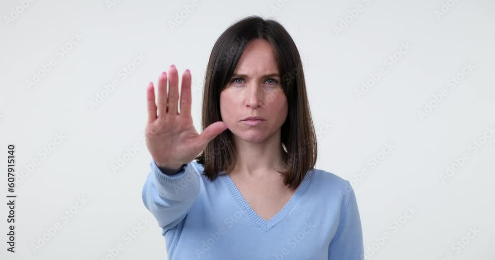 A serious-looking Caucasian woman stands against a white background and makes the stop gesture by extending her palm in front of her. She convey a sense of seriousness and authority. A serious-looking Caucasian woman stands against a white background and makes the stop gesture by extending her palm in front of her. She convey a sense of seriousness and authority.