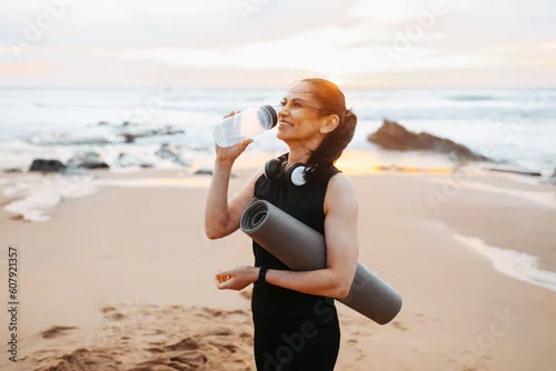 Obraz Smiling mature european woman in sportswear with mat, drinks bottle of water, enjoy workout in morning