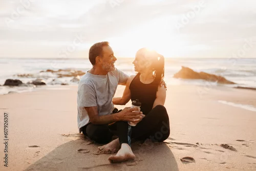 Obraz Cheerful mature european husband hugs wife in sportswear, enjoy workout with bottle of water