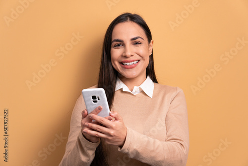 cheerful brazilian woman watching video and photos on mobile smartphone in all beige colors. communication, app, connection concept.