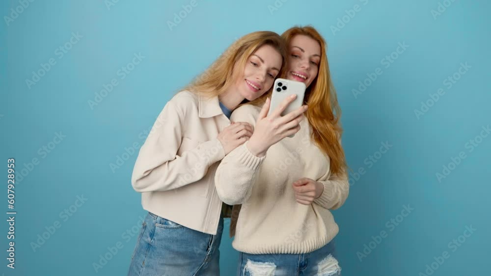 Selfie, friends, and woman posing with phone, peace sign for social media post. Two women sister, fashionable with mobile smartphone friendly smiling, taking profile picture, studio blue background Selfie, friends, and woman posing with phone, peace sign for social media post. Two women sister, fashionable with mobile smartphone friendly smiling, taking profile picture, studio blue background