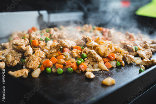 Chicken, peas, carrots, and onions cooking on a griddle outside on a campsite photo