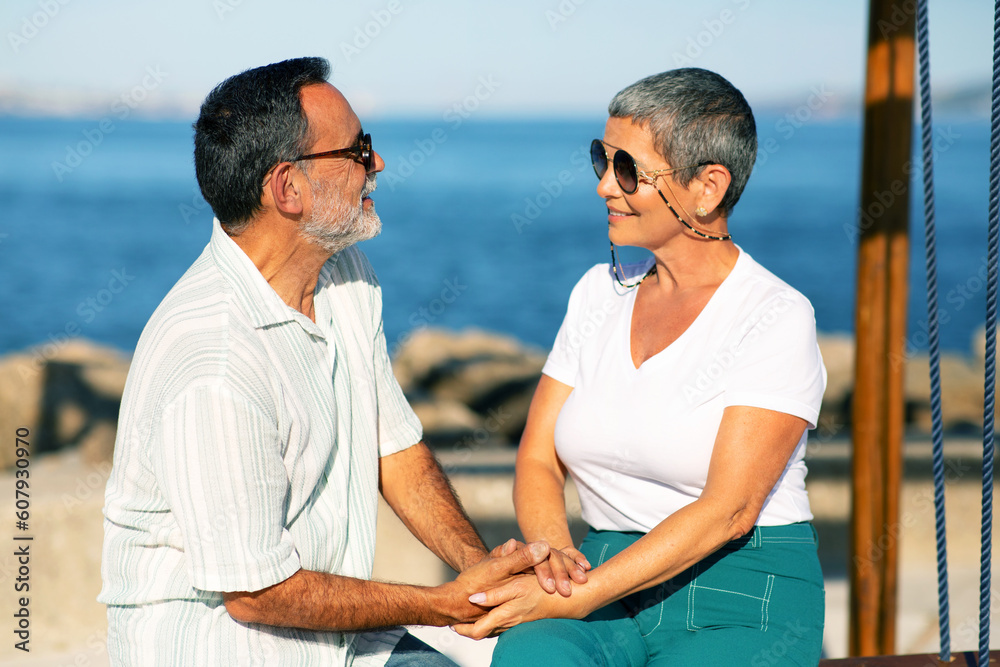 Retired Couple Holding Hands Sitting On Swings By The Sea
