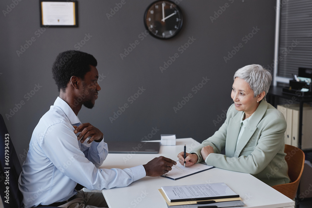 Side view portrait of smiling senior woman signing contract at job interview, copy space Side view portrait of smiling senior woman signing contract at job interview, copy space