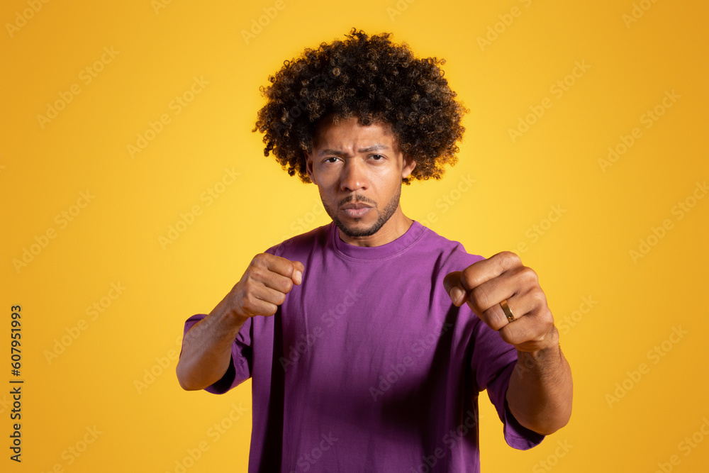 Serious confident mature black curly man wrestler boxer with fists ready to fight isolated on yellow background