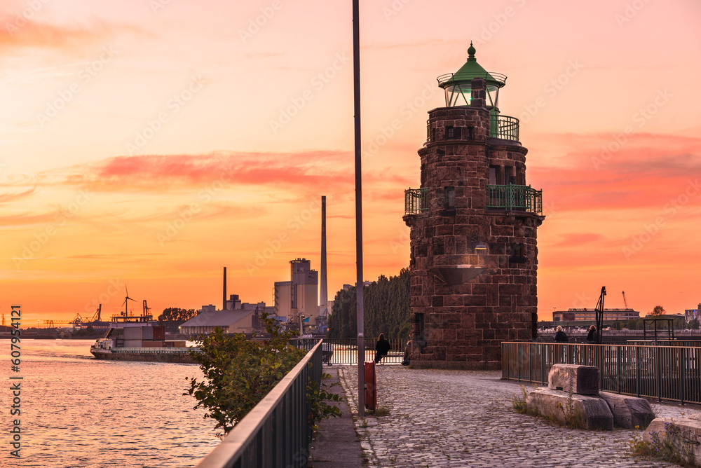Stunning summer sunset over a historic old stone lighthouse at the end of a cobblestone pier on a river harbour
