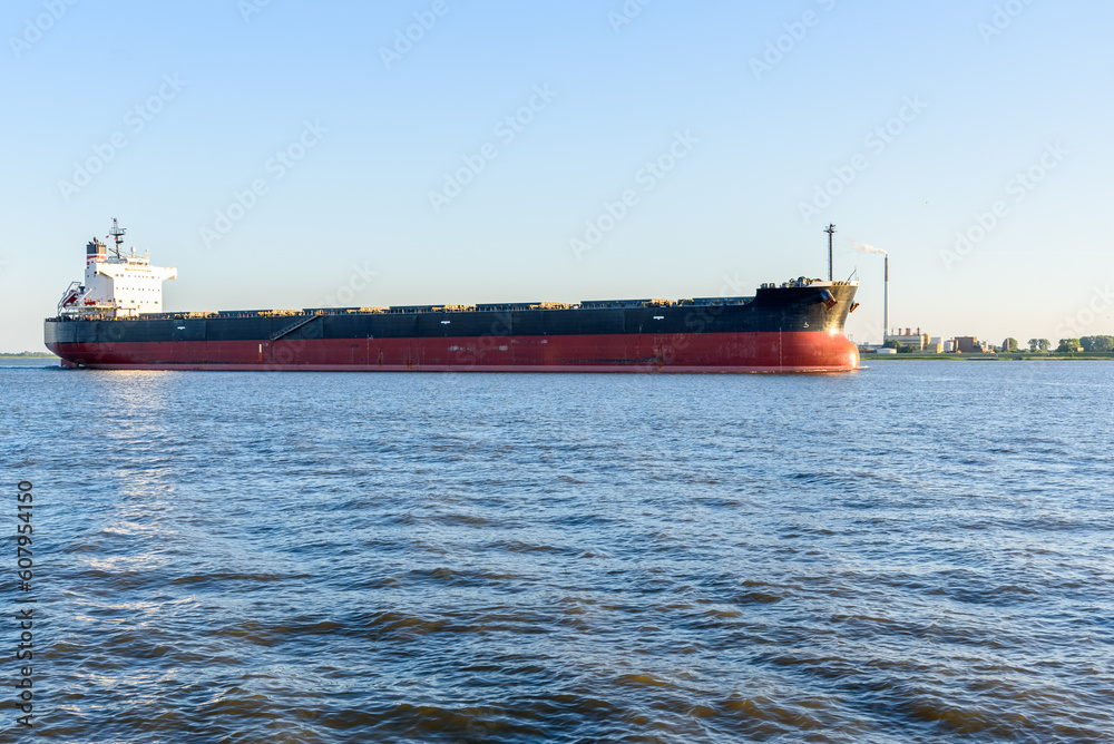 Large bulk carrier ship leaving a river harbour at sunset in summer Large bulk carrier ship leaving a river harbour at sunset in summer