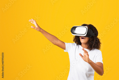 Cheerful shocked surprised adolescent curly black girl in white t-shirt and vr glasses touches empty space