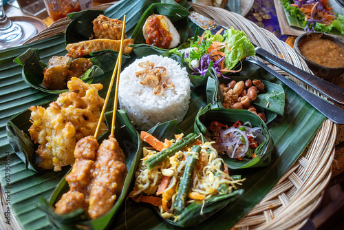 An Indonesian dinner consisting of small dishes including satay, rice, tempeh, and salads. photo