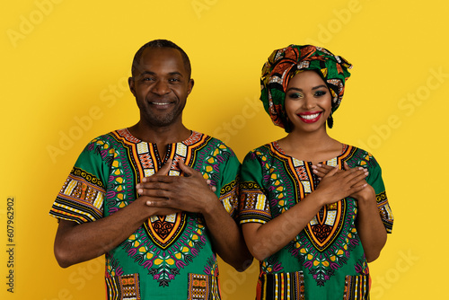 Cheerful african lovers in traditional costumes holding hands on chest