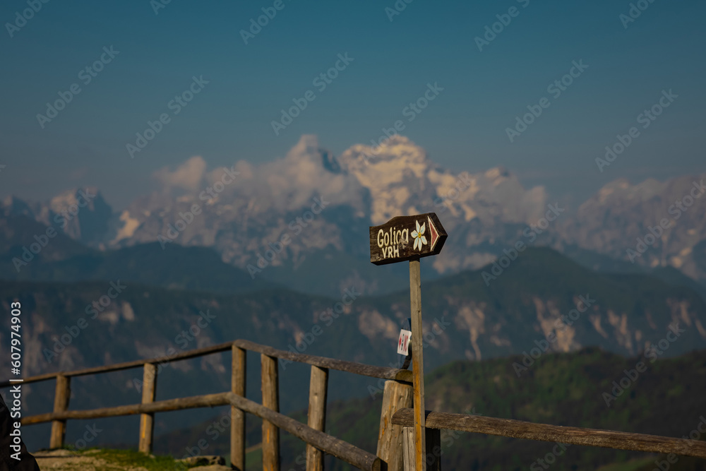 Wooden board sign leading towards the peak of Golica mountain known by its famous daffodil flowers blooming in the spring. Mount triglav in the background. Wooden board sign leading towards the peak of Golica mountain known by its famous daffodil flowers blooming in the spring. Mount triglav in the background.