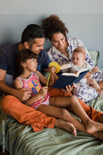 young latin family with children reading a book together on bed at home in Mexico Latin America, hispanic people with baby
