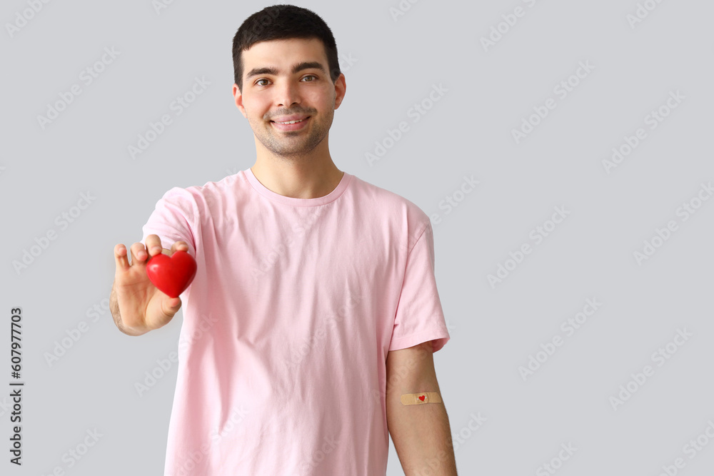 Young blood donor with applied medical patch and heart on light background Young blood donor with applied medical patch and heart on light background
