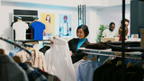 Asian customer examining formal clothes on hangers and buying new collections from retail shop. Young adult visiting clothing store to try on trendy modern merchandise, commercial activity.