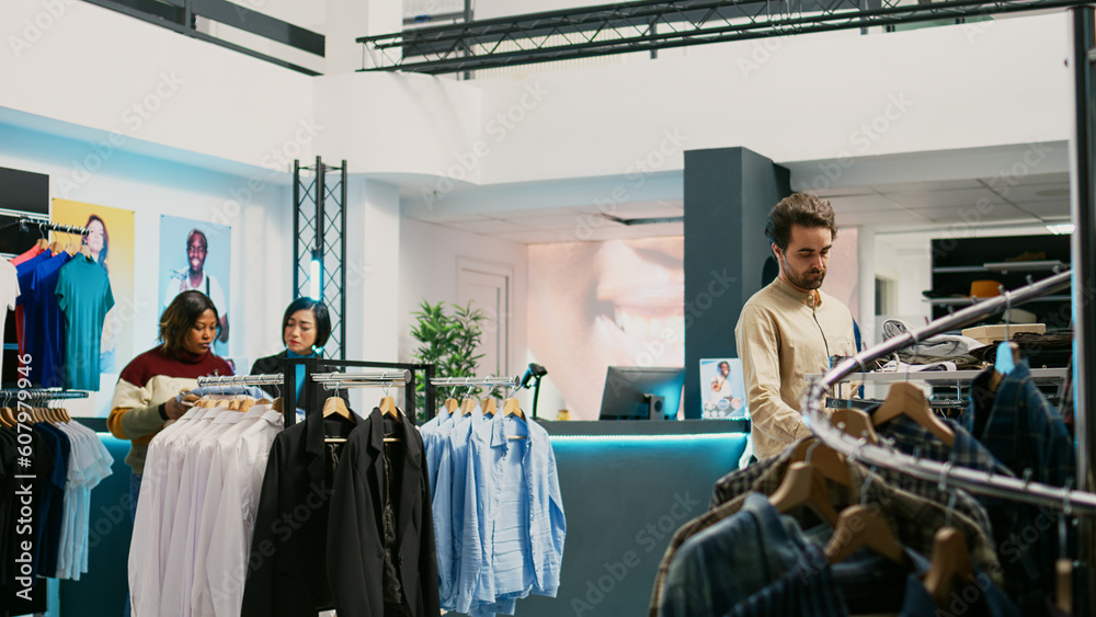 Retail worker helping customer to buy shirts at mall, diverse people looking at new fashion collections. Male client and store assistant examining trendy clothes, commercial activity.