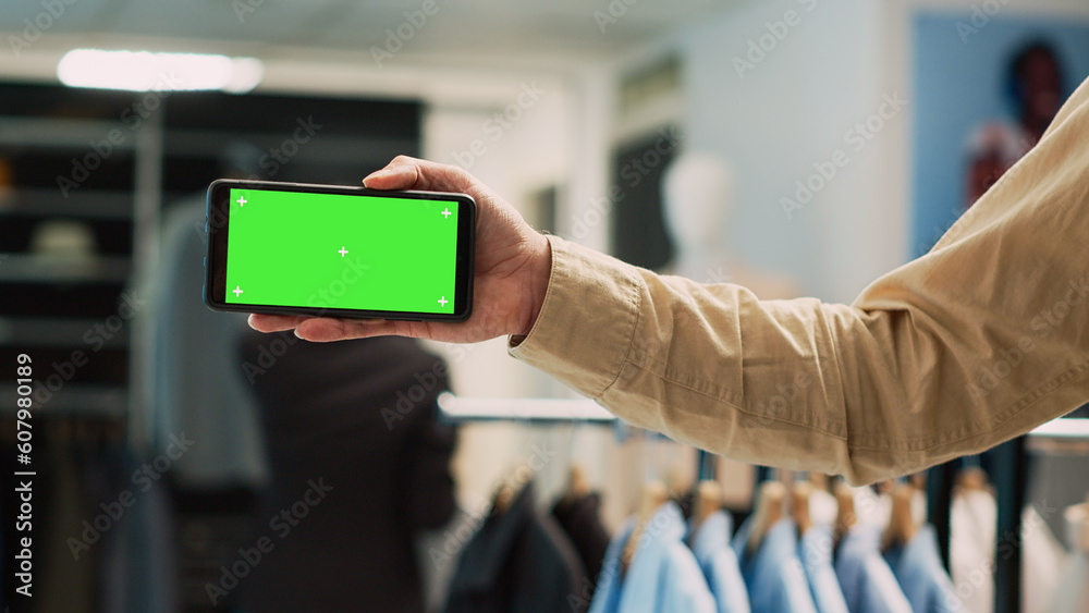 Male employee holding greenscreen on mobile phone, using isolated chroma key display for commercial activity. Store assistant showing blank mockup template on smartphone. Close up.