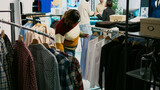 African american woman buying trendy clothes on sale, looking at fashionable modern casual wear in shopping center. Smiling young adult examining new clothing collection, small business.