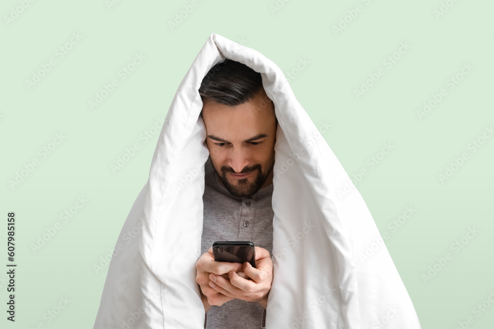 Handsome man with soft blanket using mobile phone on green background Handsome man with soft blanket using mobile phone on green background