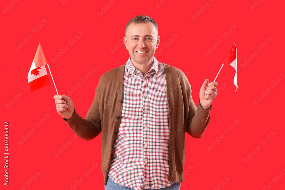 Fototapeta premium Mature man with flags of Canada on red background