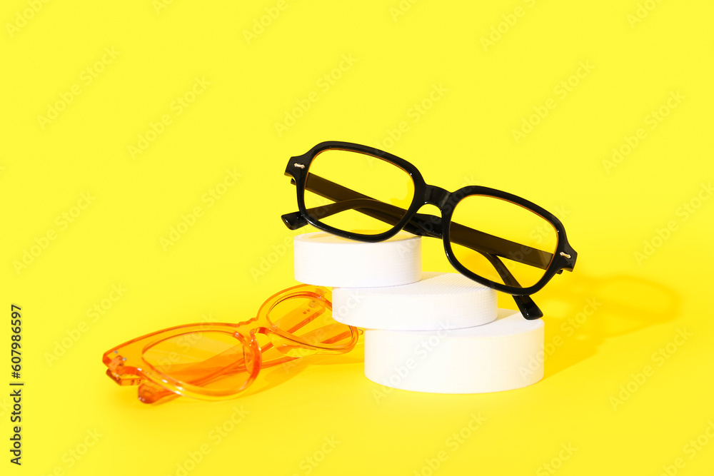 Podium with stylish sunglasses on yellow background Podium with stylish sunglasses on yellow background