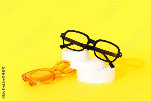 Podium with stylish sunglasses on yellow background