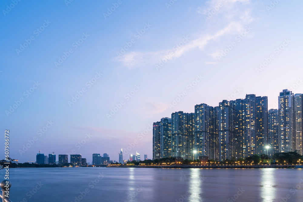 Obraz premium Tall buildings on along riverbank under cloudy sky in evening