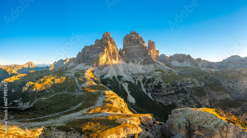 Rocky peaks of Tre Cime di Lavaredo at sunrise. Mountain landscape of wide hilly canyons and valley with serpentine roads under clear sky aerial view