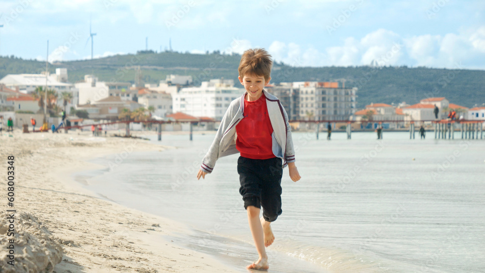 Young boy runs on the sandy beach under the bright, sunny sky, feeling carefree and alive.
