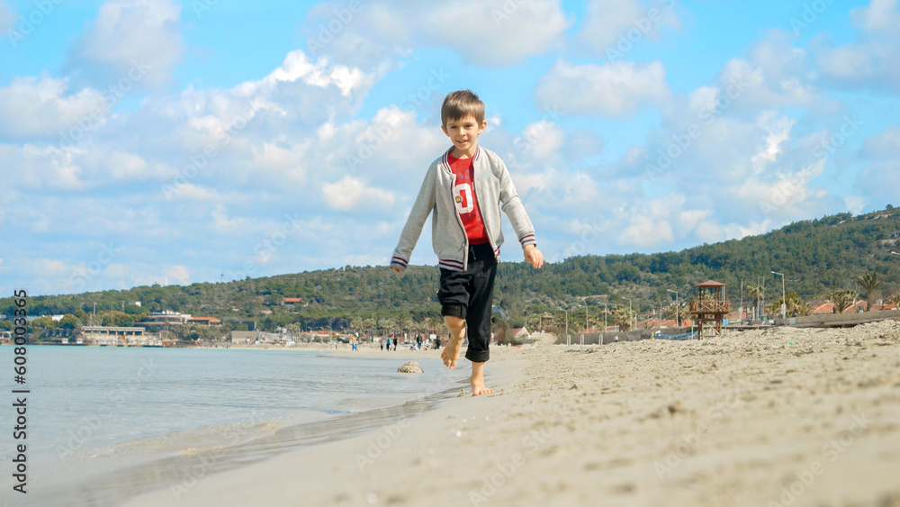 Happy laughing boy running on the sandy sea beach. Concept of tourism, travel, summer vacation