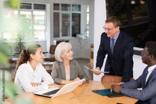 Positive partner men and women discussing a problem sitting around table in meeting room photo