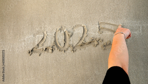 Closeup of young woman writing new year 2025 on the wet sand at sea beach photo