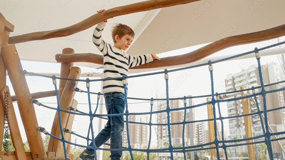 Little boy balancing on the wooden rope bridge at outdoor playground in park Little boy balancing on the wooden rope bridge at outdoor playground in park
