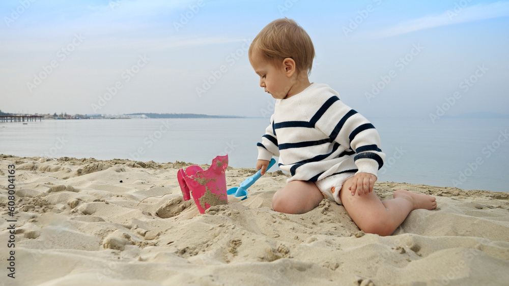 Toddler boy happily playing on the beach and digging sand with a shovel. Joy, excitement, and freedom of a family vacation, journey, and weekend. Toddler boy happily playing on the beach and digging sand with a shovel. Joy, excitement, and freedom of a family vacation, journey, and weekend.