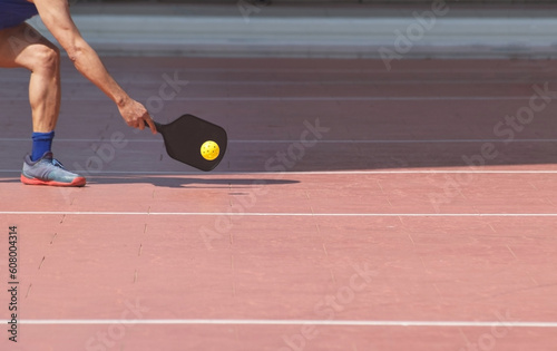 male pickleball player arm leg and paddle swinging at ball on court with copy-space 