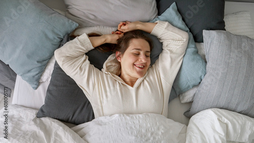 A beaming young woman wakes up in bed, stretches her arms, and lets out a contented sigh. The perfect start to a new day filled with comfort, relaxation, and healthy sleeping.