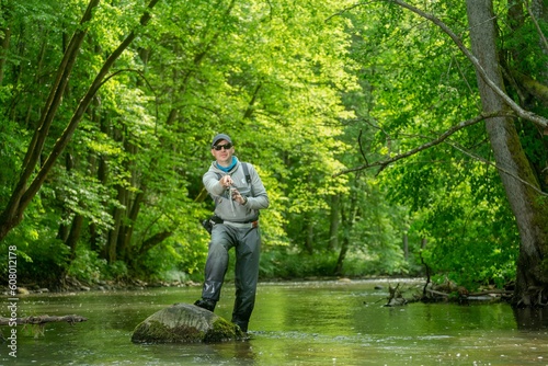 Fisherman catching brown trout on spinning tackle standing in river.