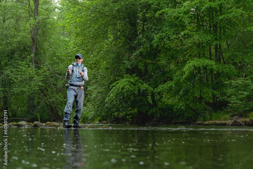 Fisherman catching brown trout on the fly standing in river.