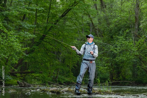 Fisherman catching brown trout on the fly standing in river.